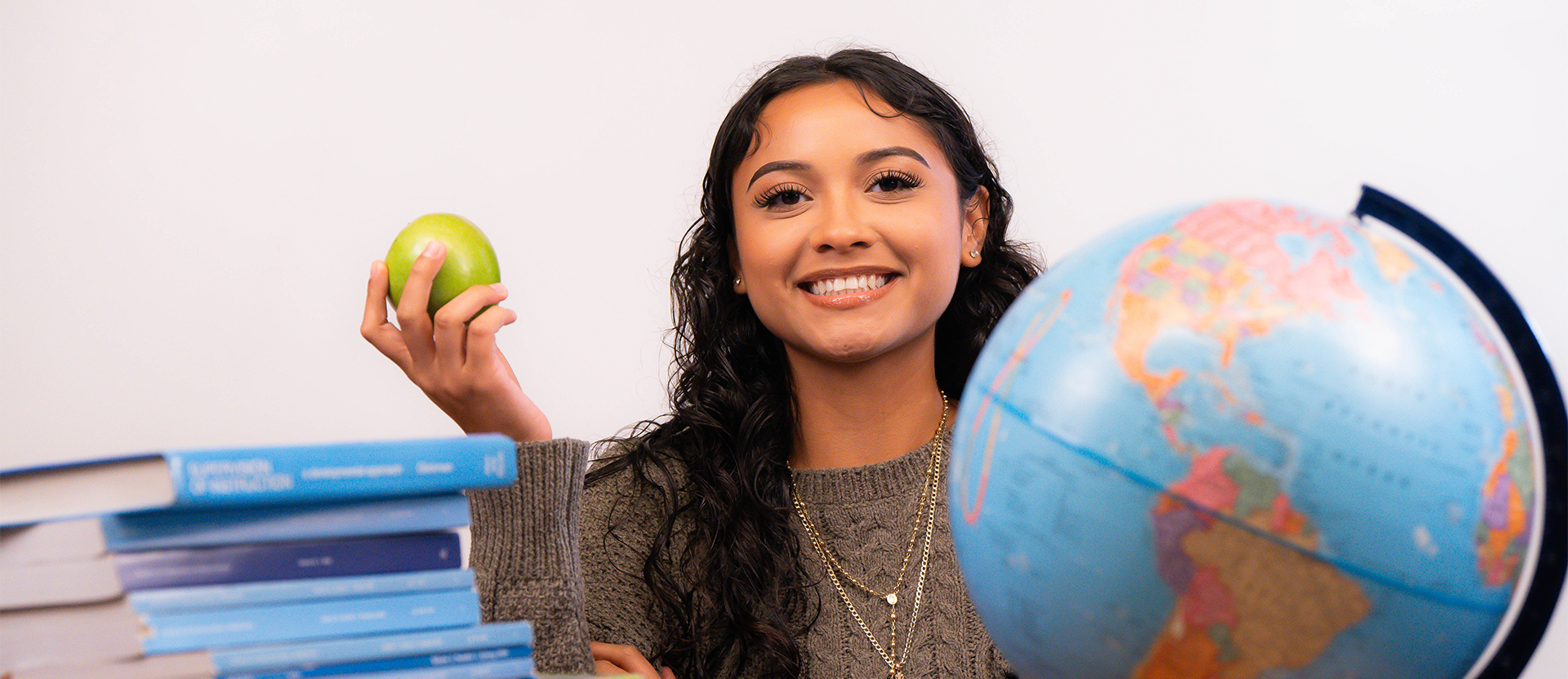Photo of female teaching student with an apple, next to a globe and stack of books