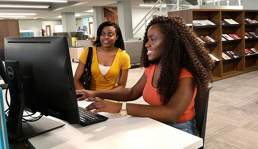 Two students working on computers in the library.